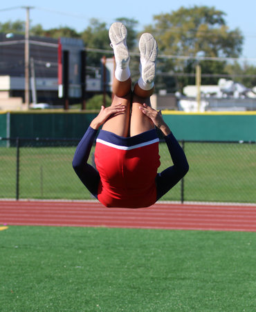 A high school cheerleader upside down flipping high in the air above a green turf field.の写真素材