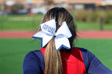 Rear view of a high school cheerleaders bow on her brunet head that has captain written on it close...