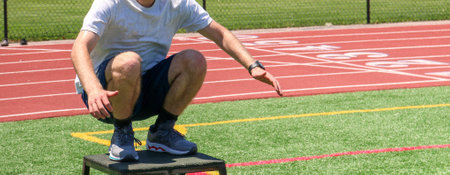 A male high school teenager landing on a ploys box in a squat position on a turf field at summer sports camp.の写真素材