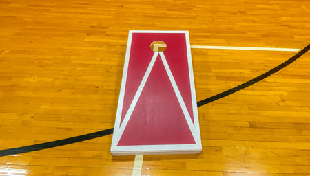 One red and white homemade cornhole board ob a high school gym floor close up.