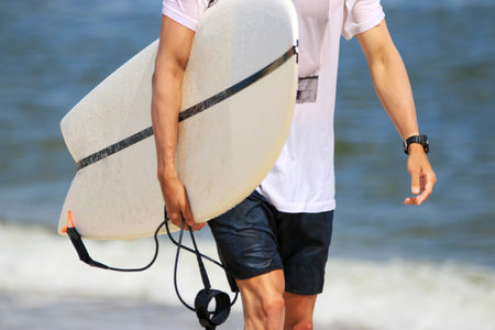 Close up of a male carrying his surfboard walking at Gilgo beach close to the ocean on Long Island.の写真素材