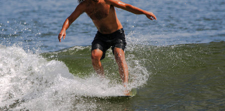 A man riding a wave standing on the front of his surfboard at Gilgo Beach on Long Island close up.