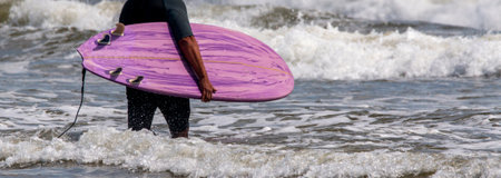 Rear view of a man carrying his purple surboard into the ocean at Gilgo Beach Long Island New York.の写真素材