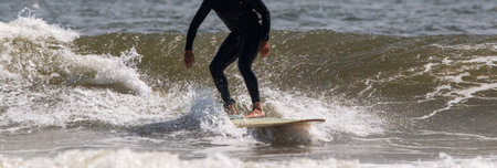 Front view of a man wearing a black wetsuit surfing at Gilgo Beach on Long Island.