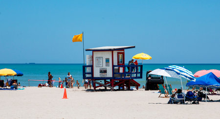 Cocoa Beach, Florida, USA - 27 June 2023: A red, blue and white lifeguard stand on the beach with umbrellas and a yellow flag at Cocoa Beach in Floridaのeditorial素材