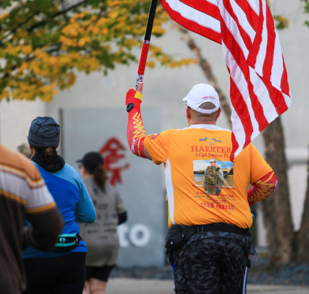 Babylon, New York, USA - 22 October 2023: A man holding an american flag in the street while running a marathon.のeditorial素材