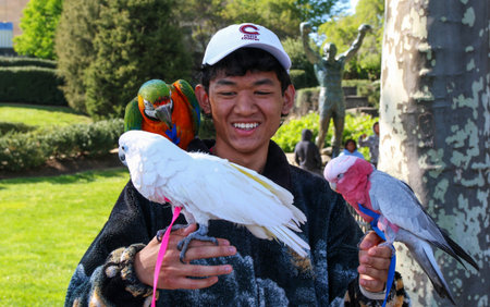 Philadelphia, Pennsylvania, USA - April 2022: A young man holding three parrots on his arm with the Rocky statue in the background in Philadelphia.のeditorial素材