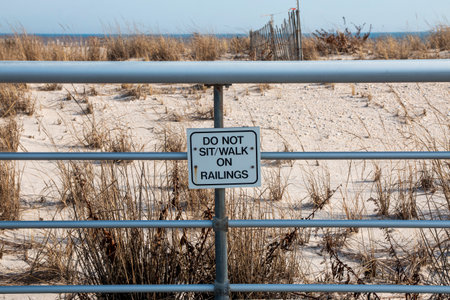 A sign that is on a metal fence soys do not sit or walk on railing in the dunes at a beach on the oceanの写真素材