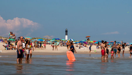 Bay Shore, New York, USA - 24 July 2021: A group of people standing on top of a sandy beach with the Fire Island Lighthouse in the Background.のeditorial素材