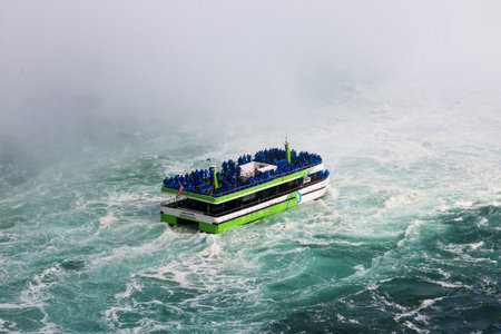 Niagara Falls, New York, USA - 30 July 2023: Green and white Niagara Falls tour boat in the mist under Horseshoe Falls with tourists wearing blue raingear,のeditorial素材