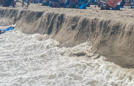 Strong waves rolling on to the beach washing away much of the sand and leaving a small cliff.