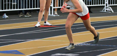 Female runner on an indoor track starting a relay race in her lane.