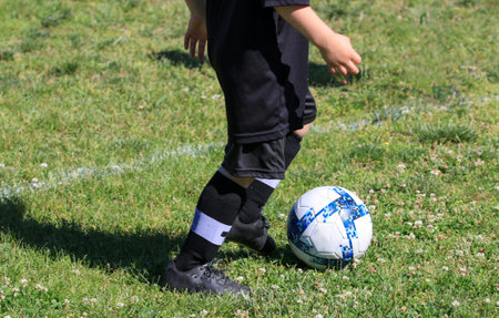 Close up of a small youth soccer player running with the ball wearing a black uniform on a grass field.の写真素材
