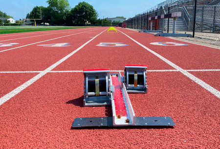 Low angle view of starting blocks in lane five on a track with yellow mini hurdles further into the...