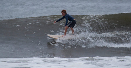 Gilgo Beach, New York, USA - 30 August 2023: One male surfer surfing a wave in the rain with...