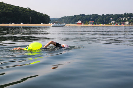 A female swimmer starting her swim out into the Long Island Sound with a beach and moored boat in...