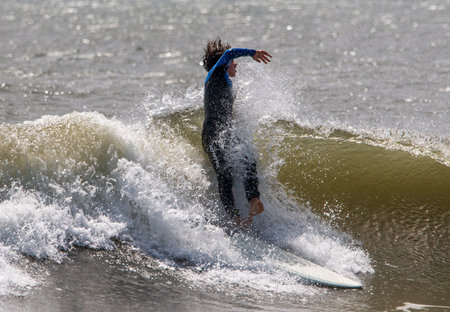 Gilgo Beach, New York, USA - 31 August 2023: Teenage boy falling and twisting off of his surfboard...