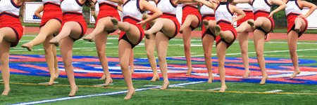 A High school kickline performing on turf field at half time of football game with their legs kicked up.の写真素材