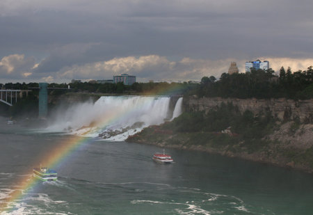 Tourists enjoy the breathtaking view of Niagara Falls with a vibrant rainbow appearing in the mist.の写真素材