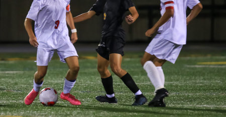 Players in white uniforms engage in a tight contest on a soccer field at night.