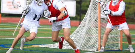 Young athletes compete energetically on a bright field during a lacrosse match.の写真素材