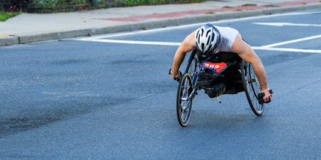 Participant races on handcycle during marathon along city streets on a sunny day.