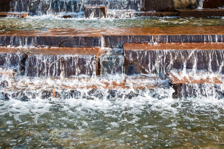 Gentle water flows down tiered stone steps, creating a peaceful atmosphere outdoors.の写真素材