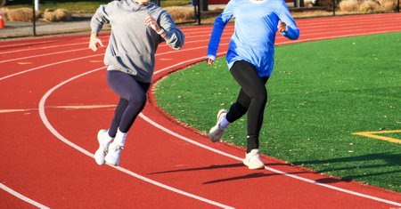 Two women wearing athletic gear run side by side on a track during a sunny day.の写真素材
