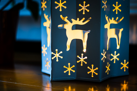 A christmas themed candle holder with candle light shining out of it, on a dining room tableの写真素材