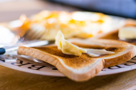 A thick slice of butter on a piece of toast on a white plate, which is also holding some fried eggs