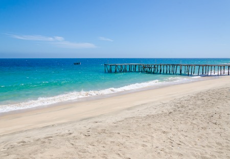 Long simple wooden jetty leading into turquoise blue ocean at small fishing village Mucuio in Angola.の写真素材