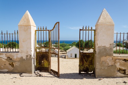 Crumbling metal gate of colonial stone wall overlooking beautiful ocean in small fishing village Mucuio in Angola.の写真素材