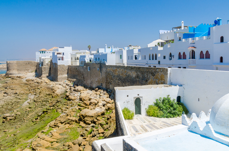 Blue and white washed buildings and ancient city wall at rocky coast of the town Asilah, Morocco, North Africa.の写真素材