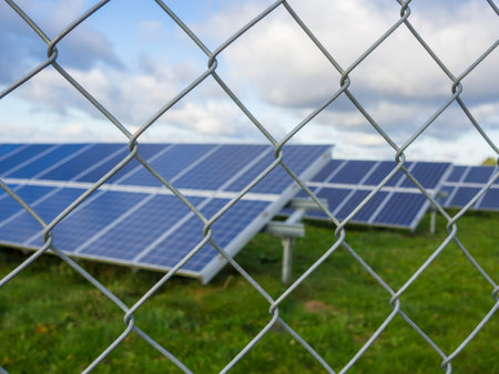 Solar panel or photovoltaic farm behind metal chainlink fence on green field with dramatic cloudy...