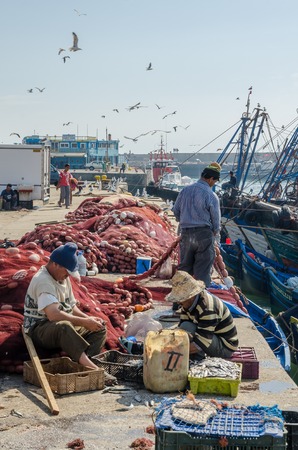 Essaouira, Morocco - September 15 2013: Unidentified local fishermen fixing nets at harbor with seagulls and boatsのeditorial素材