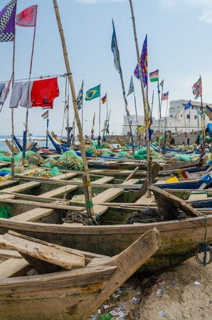 Cape Coast, Ghana - February 15, 2014: Colorful moored wooden fishing boats in African harbor town Cape Coast with colonial castle in backgroundのeditorial素材