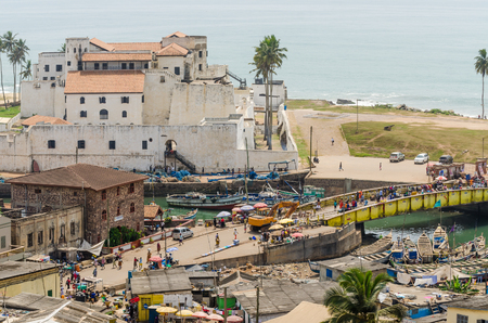 Elmina, Ghana - February 13, 2014: Colorful moored wooden fishing boats and historical colonial castle in African harbor town Elminaのeditorial素材