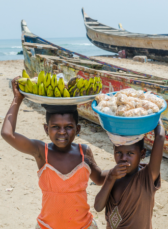 Elmina, Ghana - February 13, 2014: Two unidentified African girls balancing food on heads for sale at beachのeditorial素材