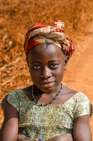 Kindia, Guinea - December 28, 2013: Portrait of unidentified African girl with red dirt road in backgroundのeditorial素材