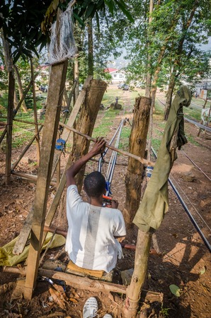 Man, Ivory Coast - January 31,2014: Unidentified African man weaving traditional blue and white Yacouba cloth outdoorsのeditorial素材