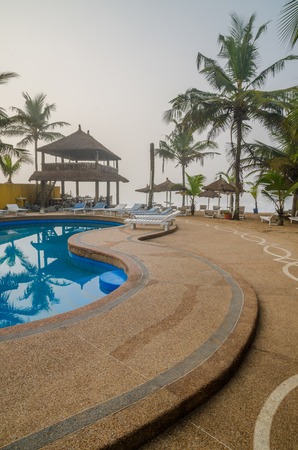 Grand-Bassam, Ivory Coast - February 02 2014: Holiday resort with pool, palm trees and thatched shelters at coastのeditorial素材