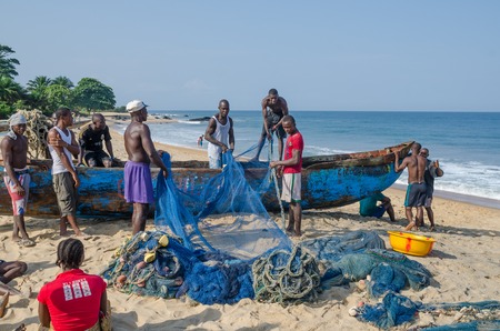 Robertsport, Liberia - January 26, 2014: Fishermen sorting nets on wooden boat at beachのeditorial素材