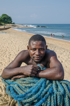 Robertsport, Liberia - January 26, 2014: Portrait of African fisherman leaning on nets at beachのeditorial素材