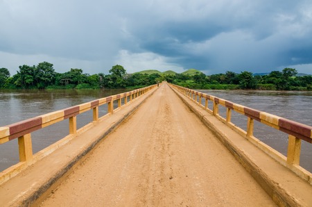 Simple dirt road bridge over tropical river with dramatic clouds in Republic of Congo, Africaの写真素材