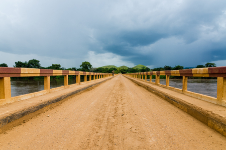 Simple dirt road bridge over tropical river with dramatic clouds in Republic of Congo, Africaの写真素材