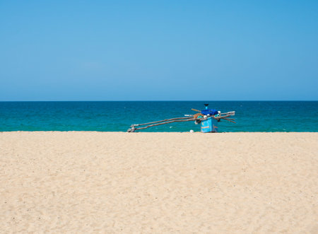 Traditional wooden fishing boat on empty beach against clear blue sky and sea, Kallady Beach,...