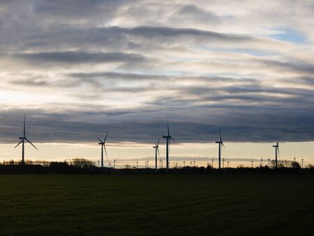 Silhouette of wind turbines or windmills creating electricity from wind power on field at sunset, Nordfriesland, Germany.の写真素材