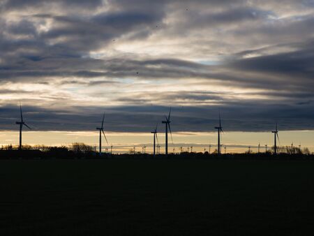 Silhouette of wind turbines or windmills creating electricity from wind power on field at sunset, Nordfriesland, Germany.の写真素材