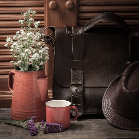White and purple flower in vase place in front of leather hat and bag with wooden backgroundの写真素材