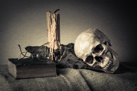 Still life with skull near old book and yellow candle on the logの写真素材